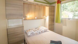 Un llit individual amb capçalera, una finestra amb cortines i una prestatgeria integrada a la paret sobre el llit.