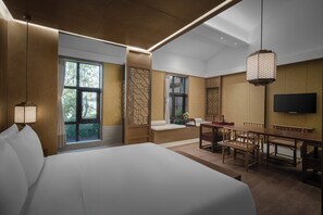 Ein modernes Hotelzimmer mit einem großen Bett, einem Essbereich mit Holzmöbeln, einem an der Wand befestigten Fernseher und großen Fenstern mit Blick ins Freie.