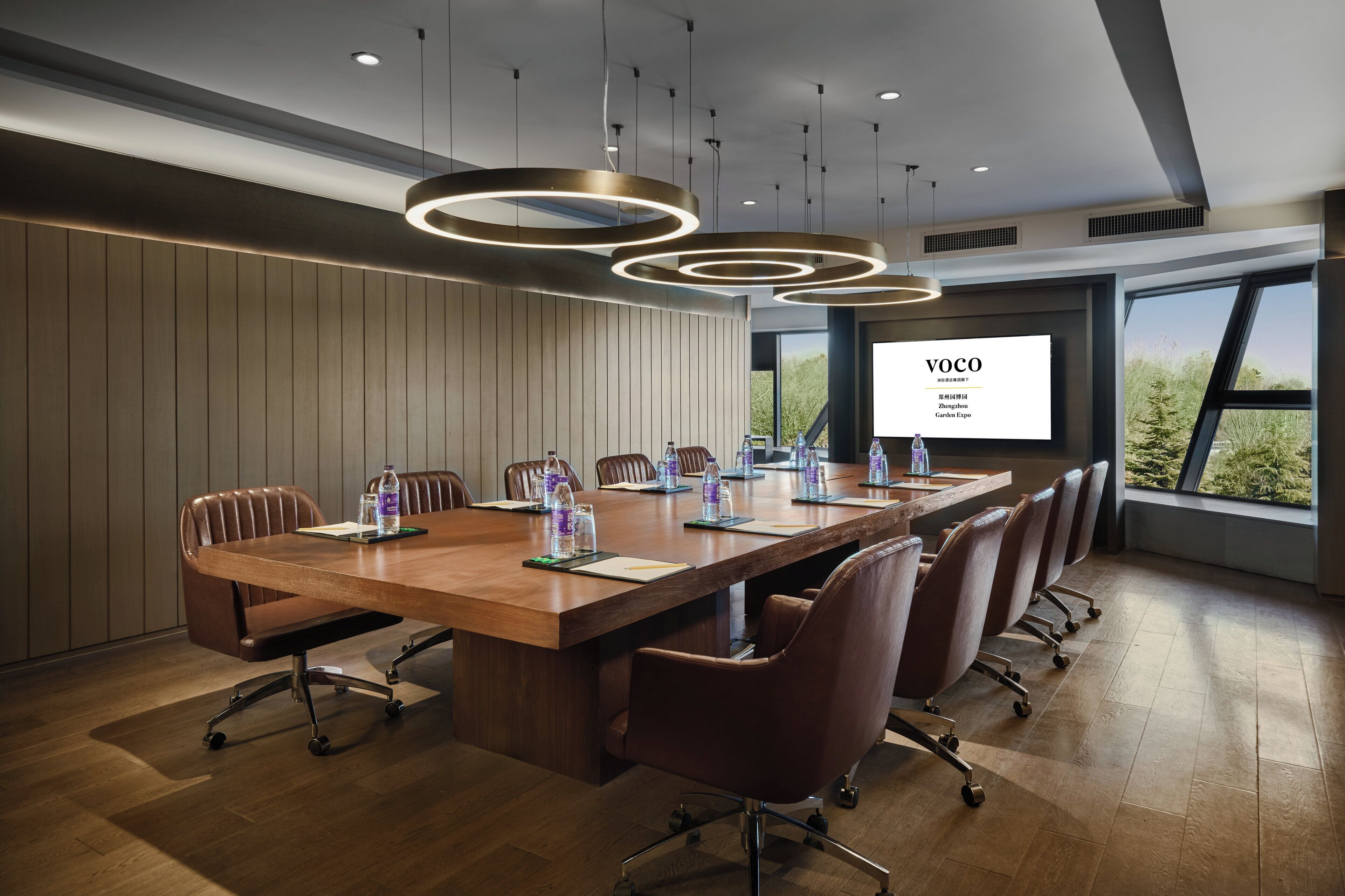 A conference room with a long wooden table, brown leather chairs, and a large screen displaying "VOCO".