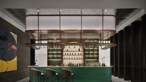 En bar med en grøn bardisk, flere hylder med flasker og tre barstole.