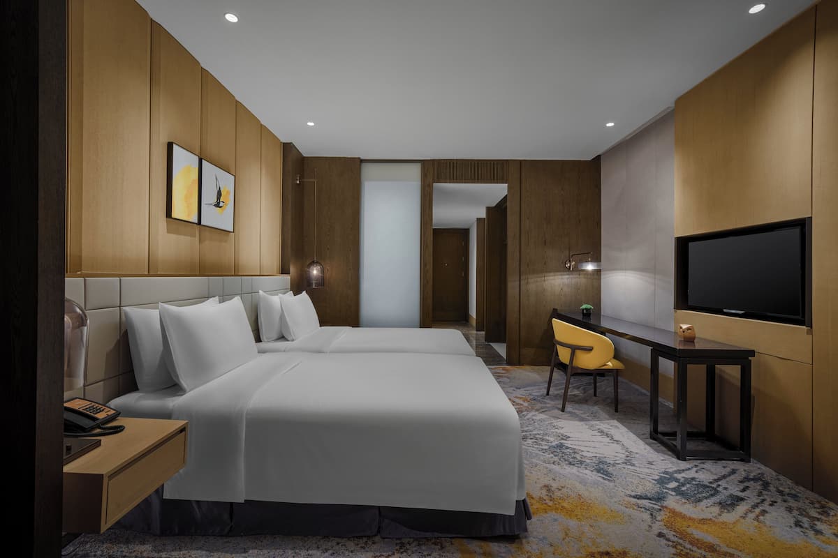 Una habitación de hotel moderna con una cama grande, mesitas de noche, un escritorio con silla, un televisor de pantalla plana y obras de arte en las paredes.