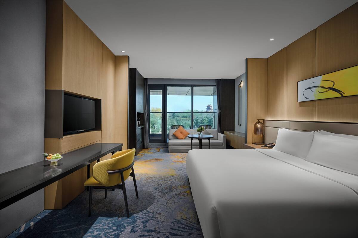 Habitación de hotel moderna con una cama grande, un escritorio con silla, un televisor y un balcón con vistas a una pagoda.