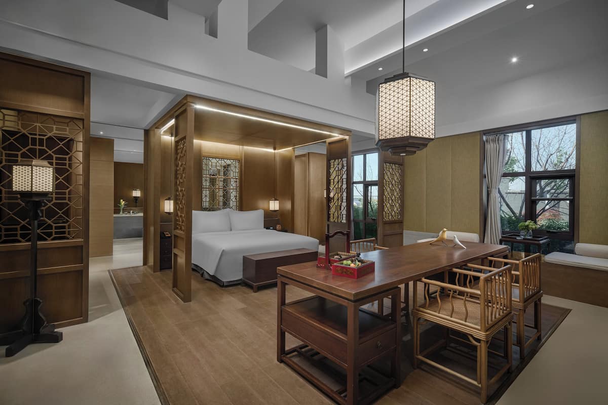 Una habitación de hotel moderna con cama, mesita de noche y una zona de comedor con sillas.