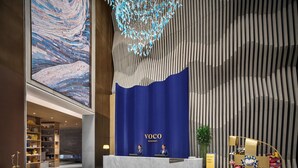 Un área de recepción con fondo azul, dos recepcionistas, una barra de mármol y un cuadro abstracto de gran tamaño.