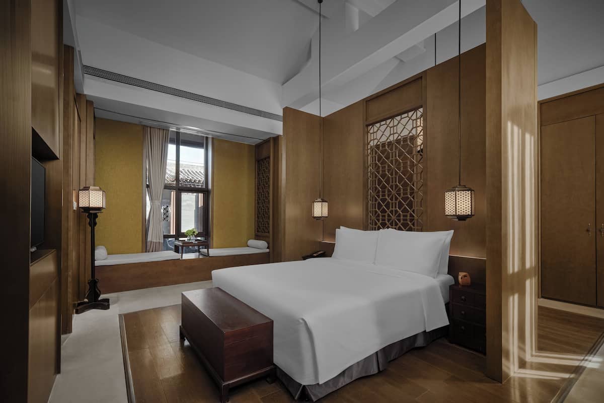 Una habitación de hotel moderna con una cama grande, lámparas de noche, suelo de madera y vistas al exterior.