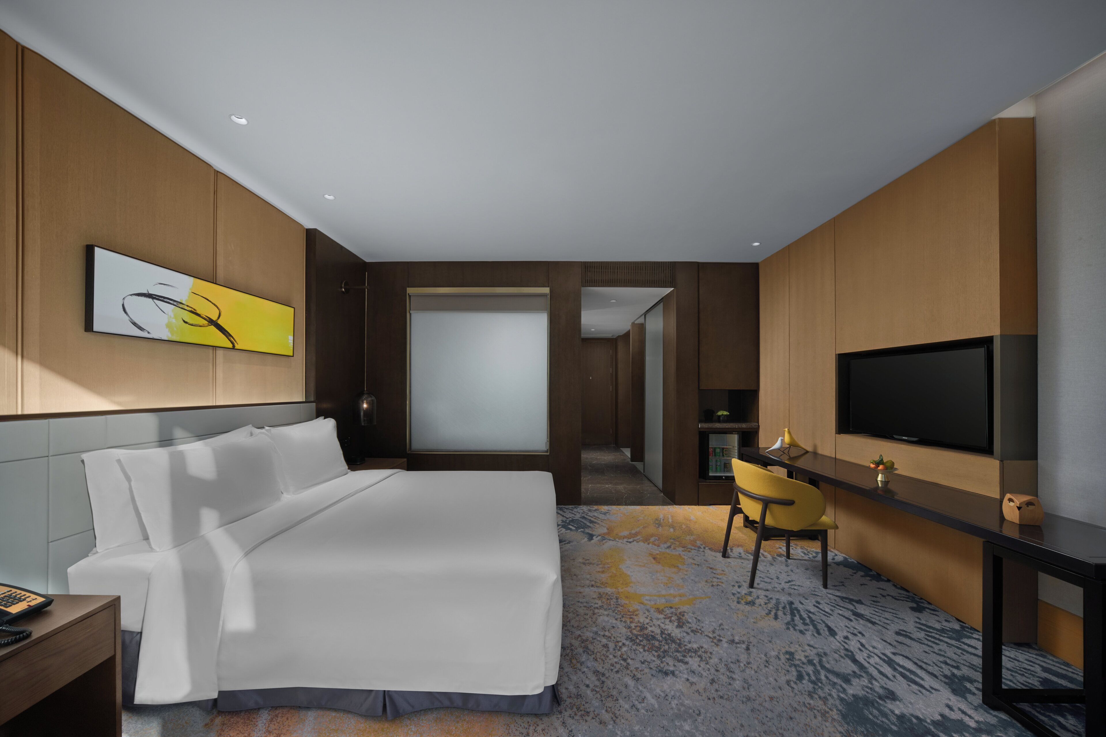 A hotel room with a bed, a desk with a chair, a television, and a large window.