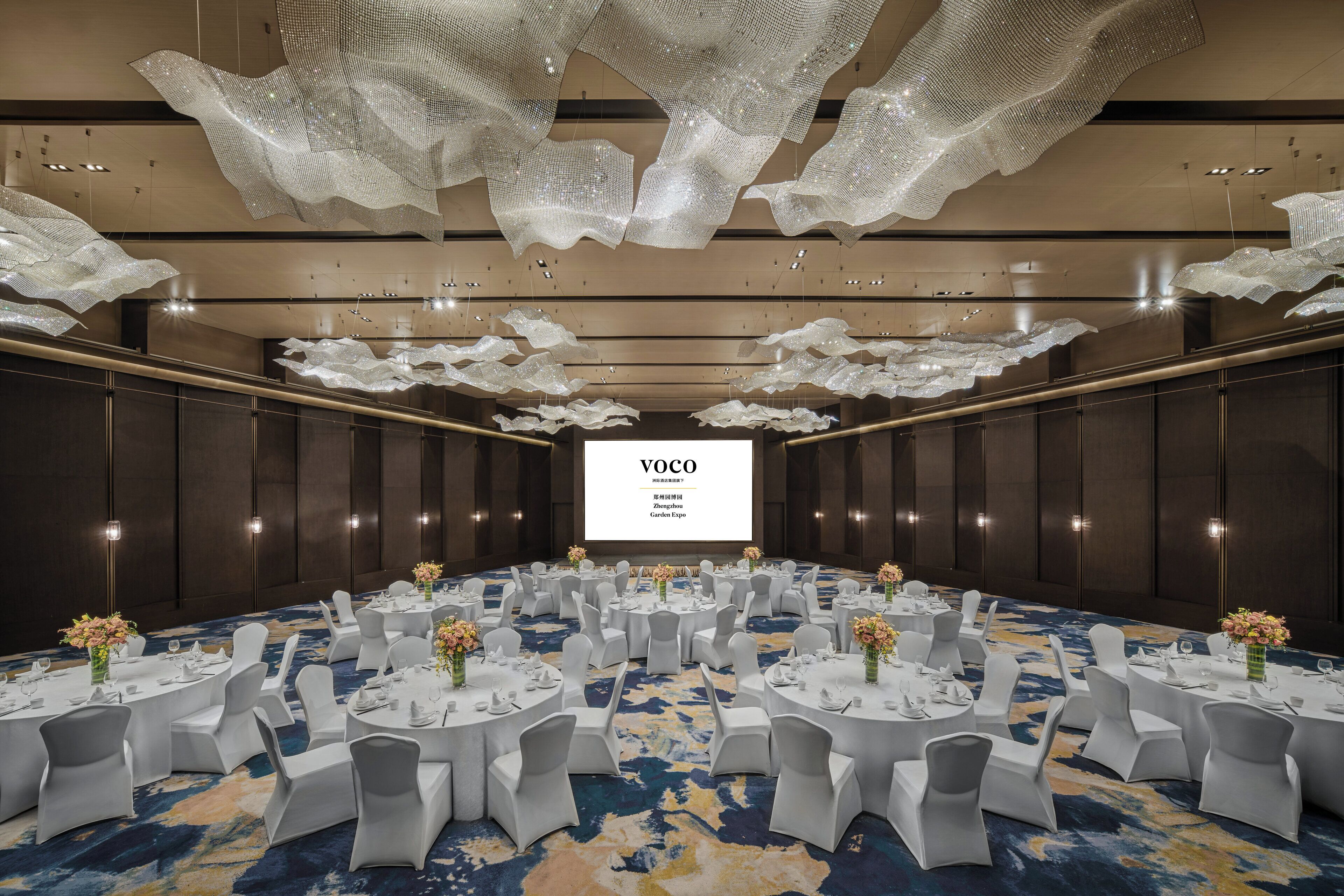 A conference room with round tables, white chairs, and a large screen displaying "VOCO".