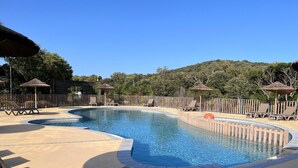 Une piscine entourée d’une clôture en bois et d’arbres, avec des chaises longues et des parasols.
