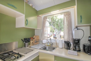 Uma cozinha compacta com fogão a gás, pia, cafeteira e janela com cortinas.