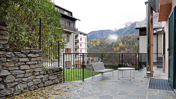 Une terrasse dallée de pierres, avec un banc et une table, un mur en pierre et une vue sur les montagnes en arrière-plan.