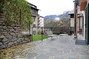 Une terrasse dallée de pierres, avec un banc et une table, un mur en pierre et une vue sur les montagnes en arrière-plan.