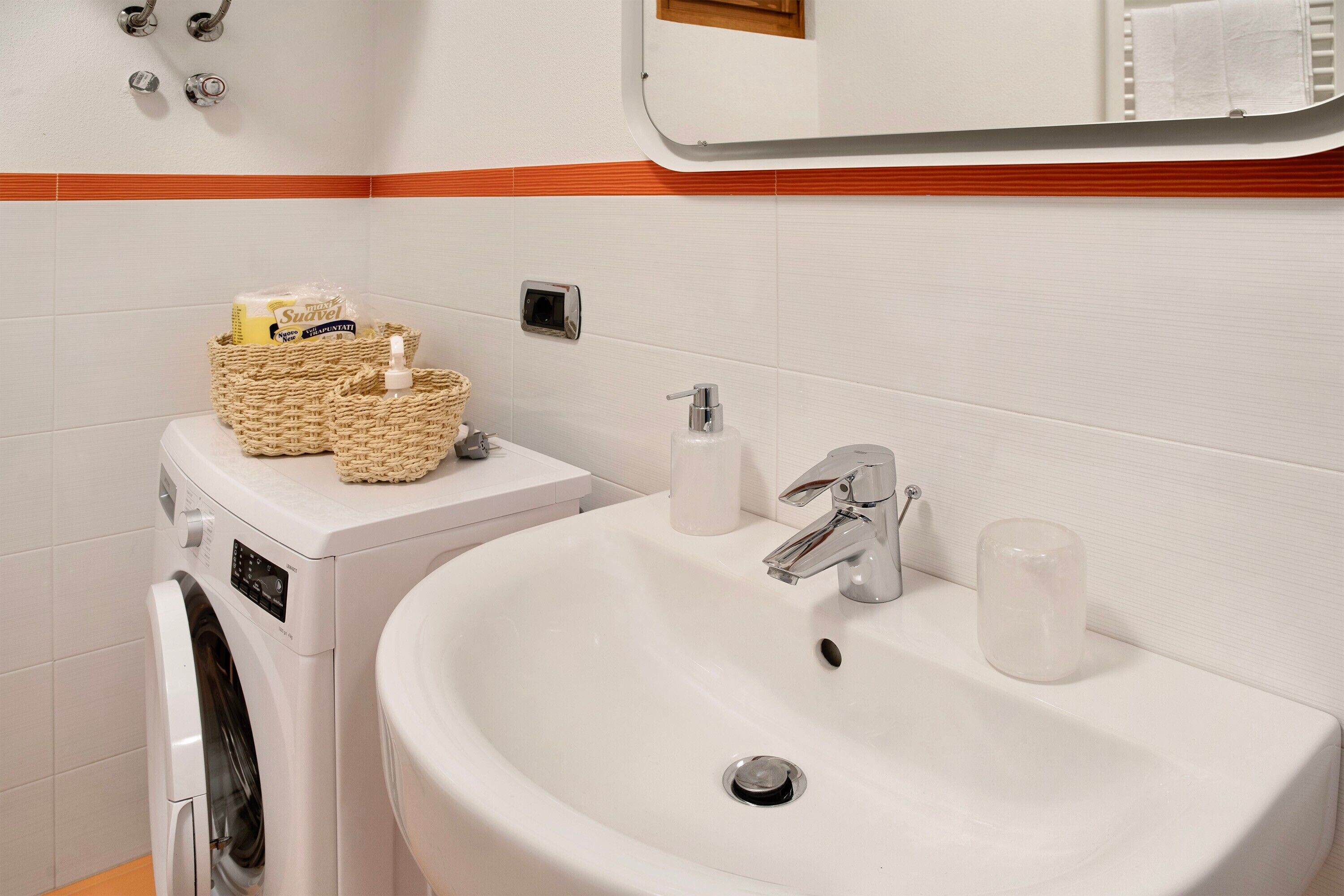 Een badkamer met een wasmachine, een wastafel met een spiegel erboven en een handdoekrek.