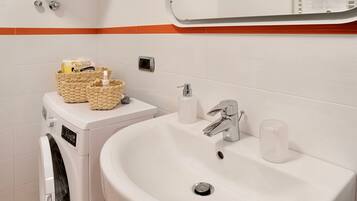 Een badkamer met een wasmachine, een wastafel met een spiegel erboven en een handdoekrek.