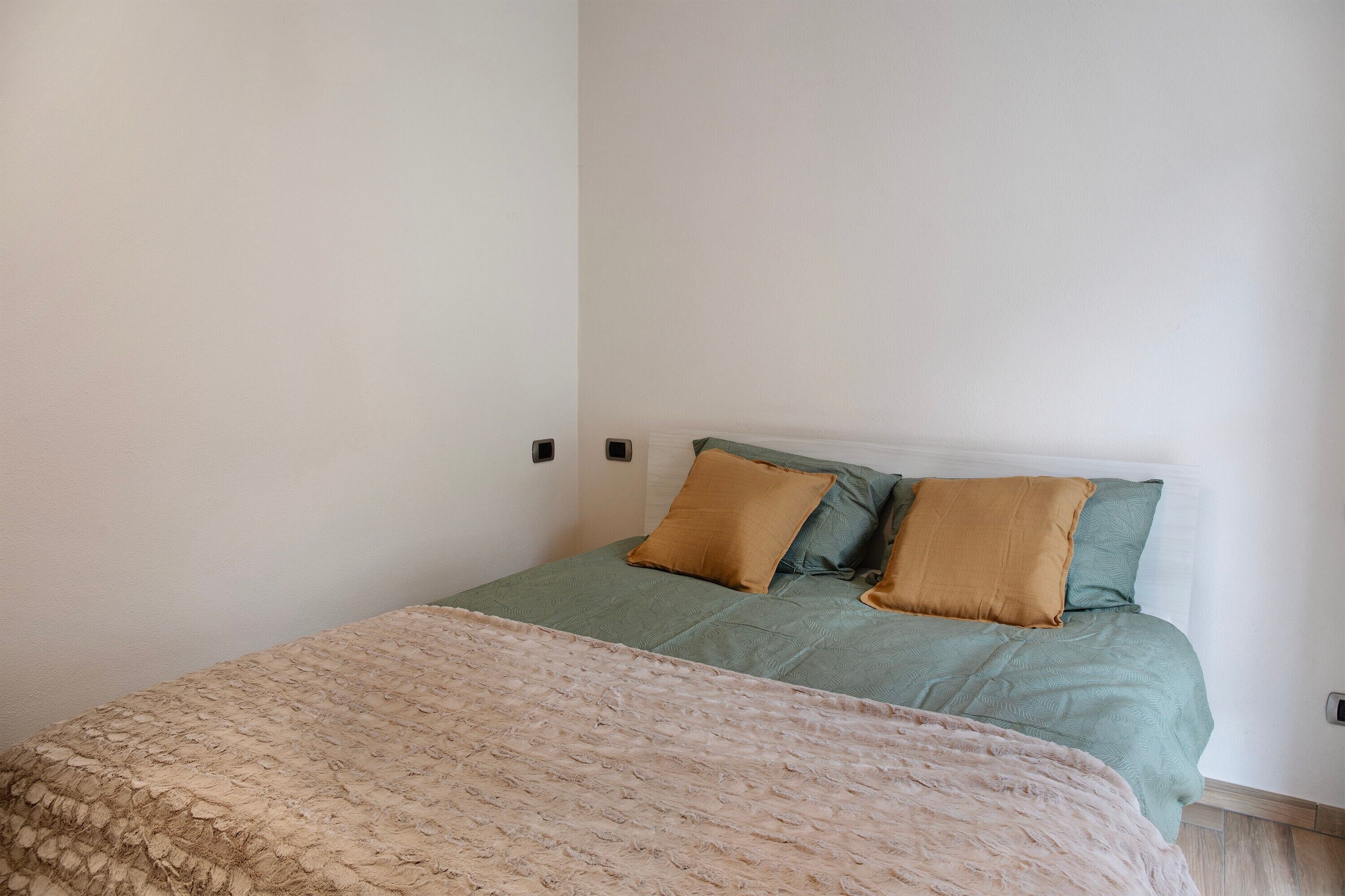 A bedroom with a bed, two pillows, a blanket, and a wall-mounted light.