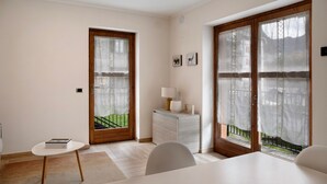 Une chambre moderne avec une porte en bois, une petite table sur laquelle se trouve un livre, une armoire blanche et une vue dégagée sur l’extérieur grâce à de grandes fenêtres.