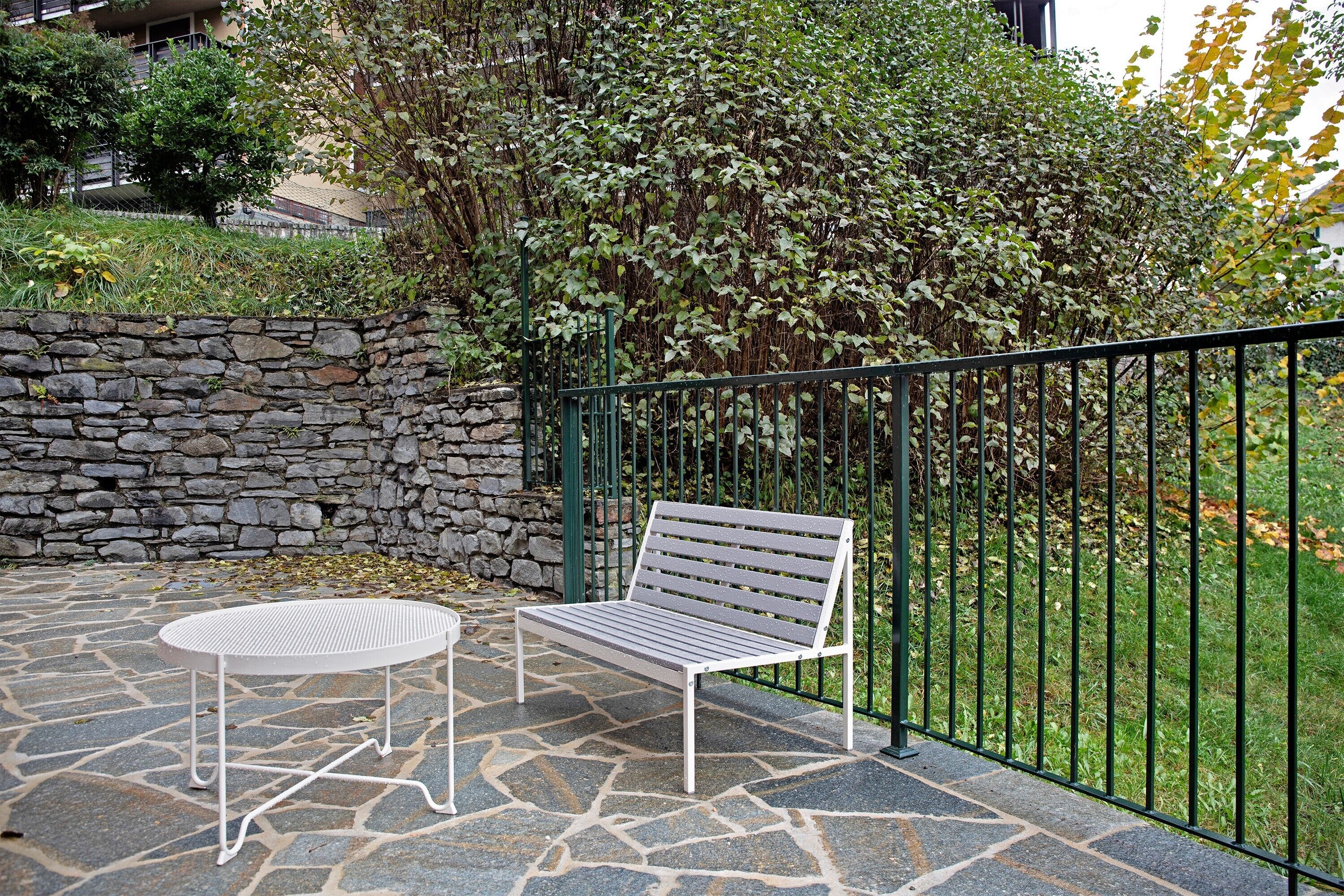 Un patio in pietra con un tavolo e una panchina in metallo, circondato da un muro in pietra e una recinzione metallica.