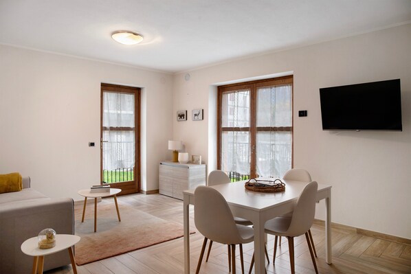 A modern living room with a dining area, large windows, a flat-screen TV, and a sofa.