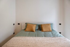 Un lit avec une couvre-lit verte et deux oreillers marron, une couverture beige et un mur blanc uni avec deux prises électriques.