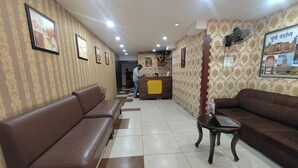 A reception area with a brown sofa, a small table with a laptop, and a reception desk. - Hotel Gargi Deluxe (Pune)