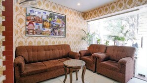 A living room with two brown sofas, a small round table, and a wall-mounted picture frame with text and images. - Hotel Gargi Deluxe (Pune)