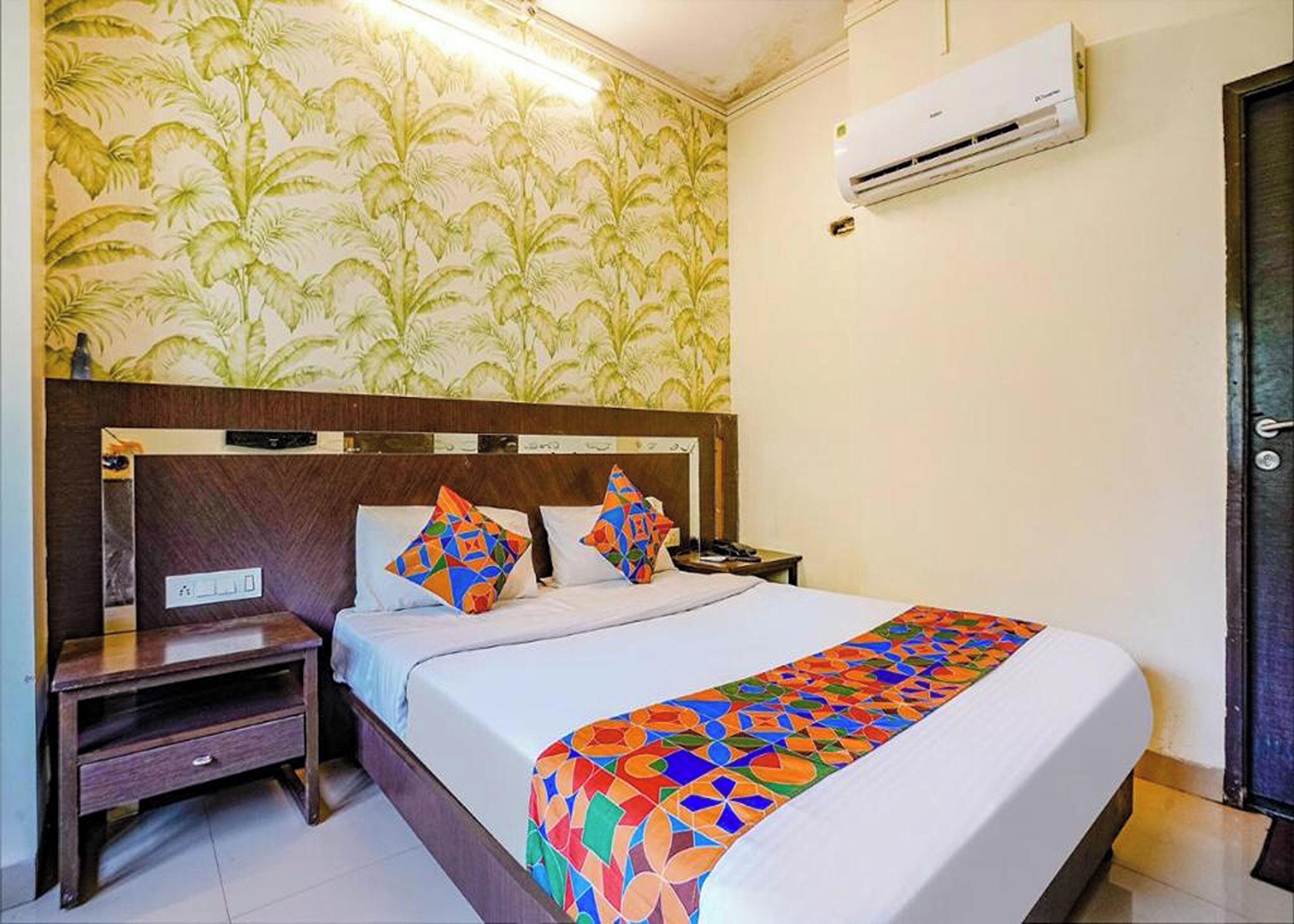Una habitación de hotel con cama, mesita de noche, aire acondicionado y una puerta.