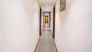 A hotel hallway with a patterned carpet, white walls, and a framed picture on the right. - Hotel Gargi Deluxe (Pune)