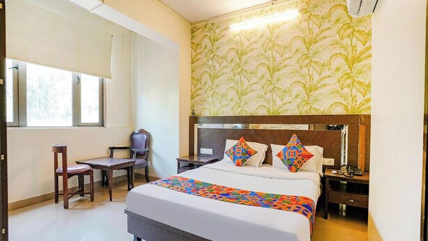 A hotel room with a large bed, a desk, a chair, and a window. - Hotel Gargi Deluxe (Pune)