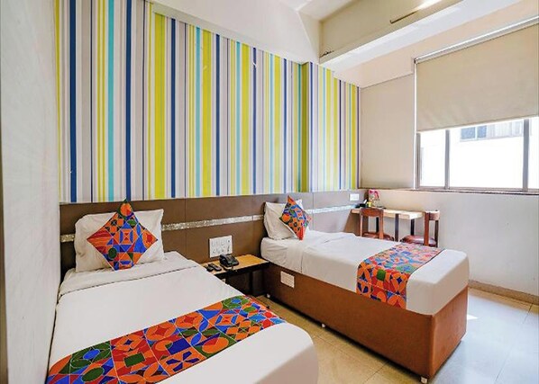 A hotel room with two beds, a small table, and a window. - Hotel Gargi Deluxe (Pune)