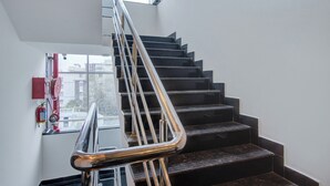 A staircase with a metal handrail and black steps, leading to a landing with a window and a fire extinguisher mounted on the wall. - Botanica Luxury Living Space, Gachibowli, Hyderabad (Hyderabad)