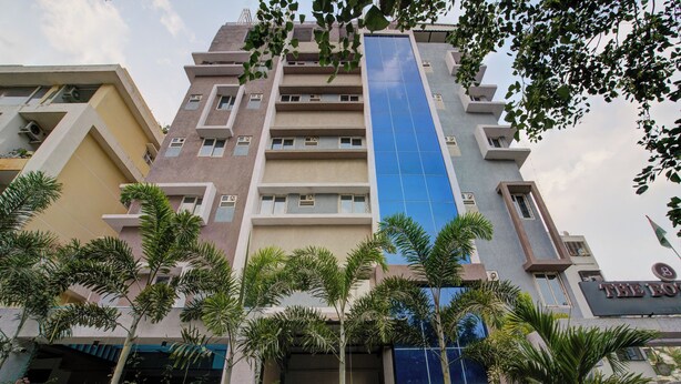 A multi-story hotel with a prominent blue glass facade, surrounded by palm trees and other greenery. - Botanica Luxury Living Space, Gachibowli, Hyderabad (Hyderabad)