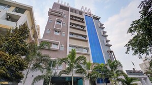 A multi-story building with a prominent blue vertical stripe, surrounded by palm trees and other greenery. - Botanica Luxury Living Space, Gachibowli, Hyderabad (Hyderabad)