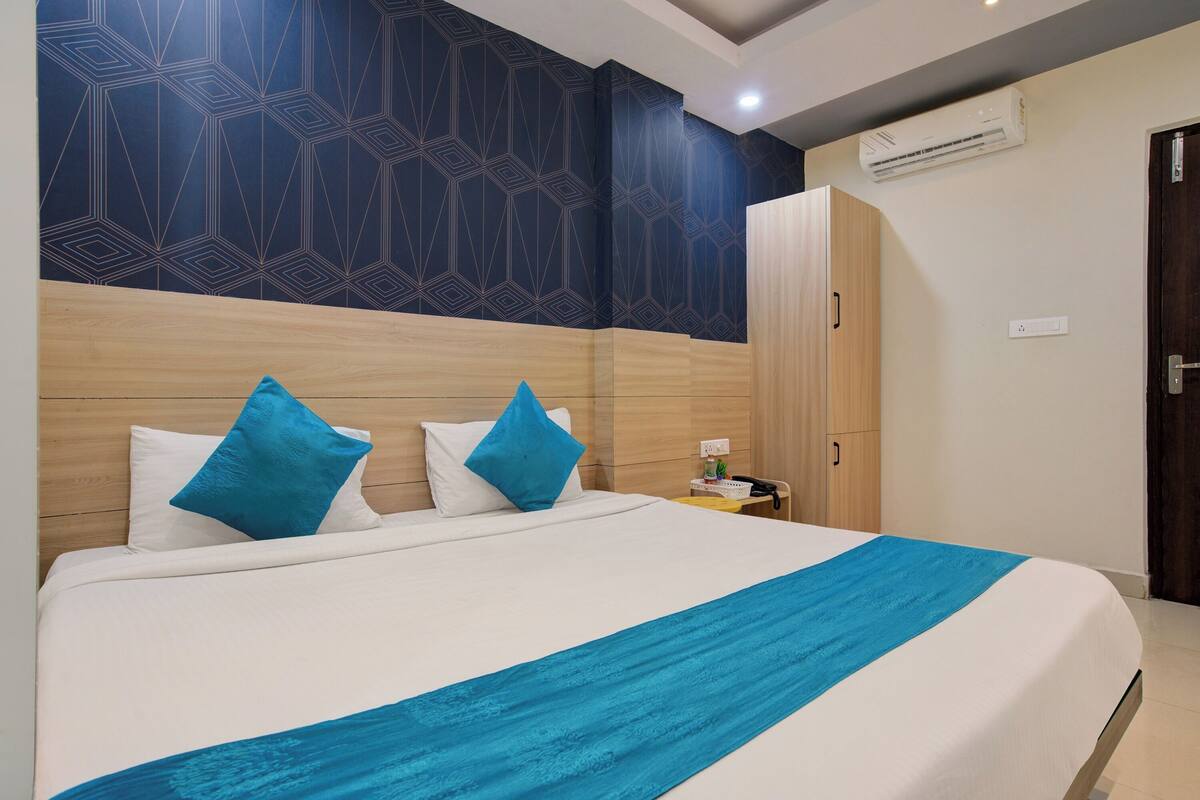 A hotel room with a large bed, two blue pillows, a white bedspread, and a blue throw.