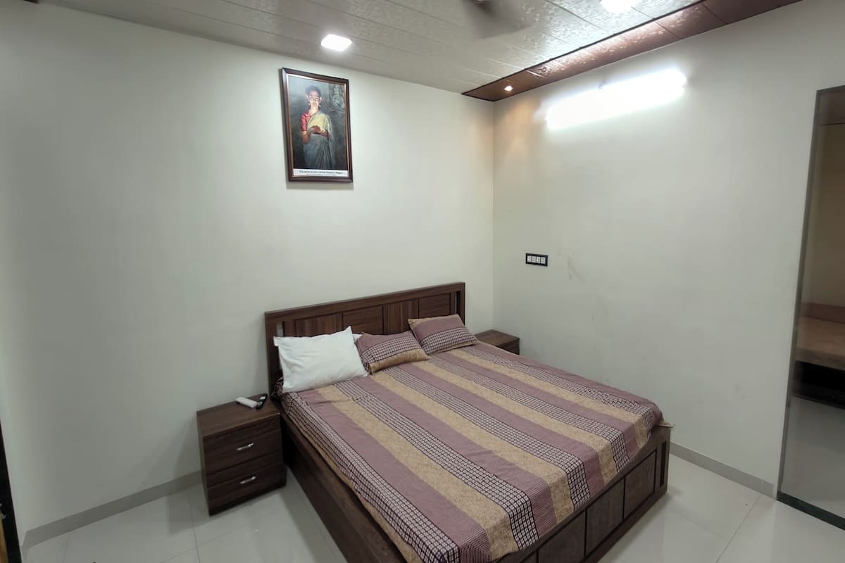 A bedroom with a wooden bed, a nightstand, a framed picture on the wall, and a ceiling light.