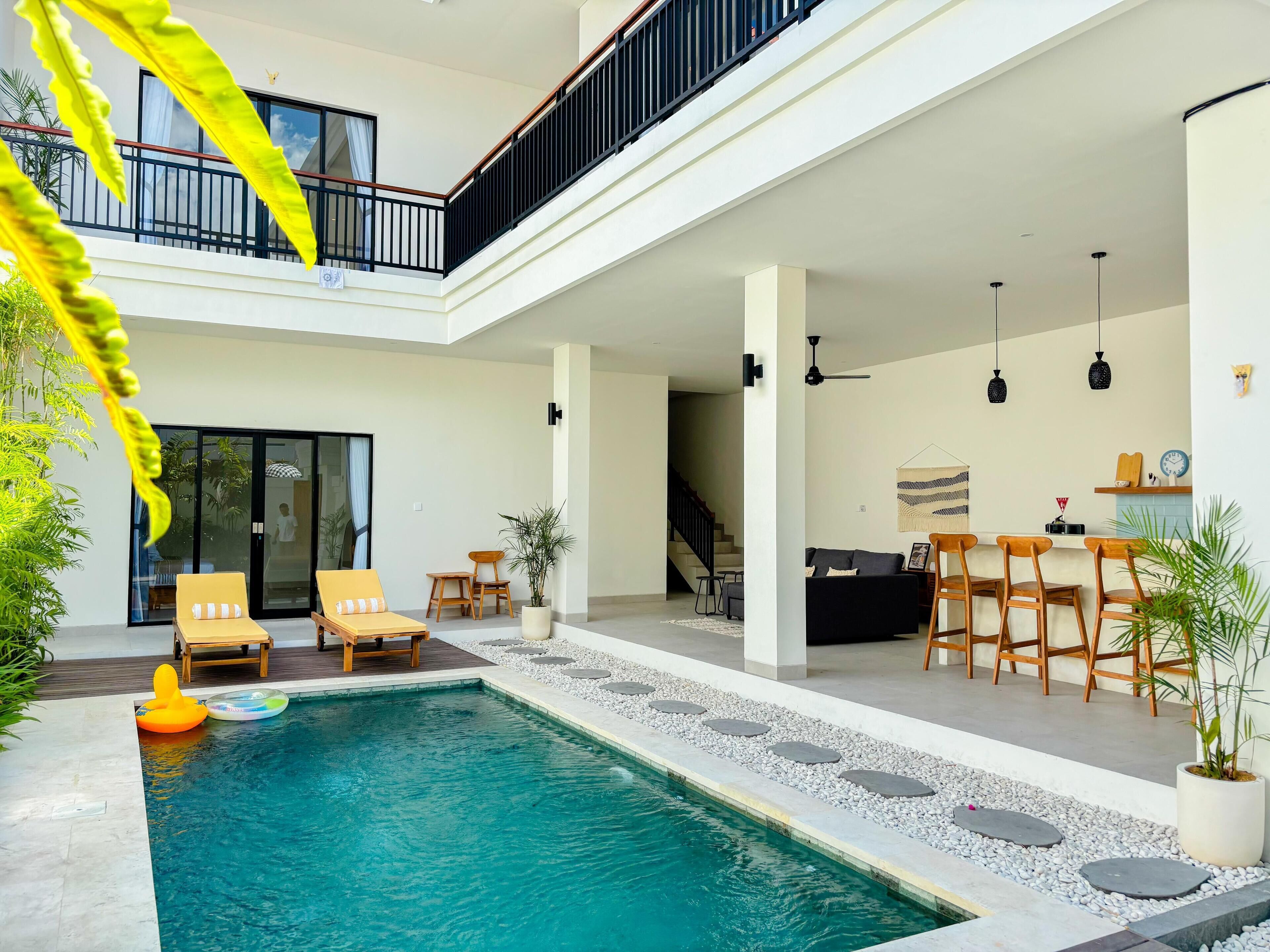 Un espace piscine intérieur moderne offrant une vue dégagée sur la piscine, des chaises longues et un coin repas avec des tabourets de bar.