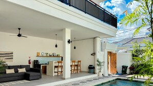 A modern outdoor living space with a pool, lounge chairs, a dining area, and a kitchen. - Villa Andra Canggu (Canggu)