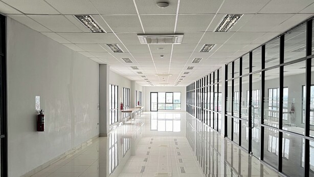 A long, well-lit corridor with reflective tiled floors, large windows on one side, and fire extinguishers mounted on the walls. - Griya Dasana Residence (Curug)