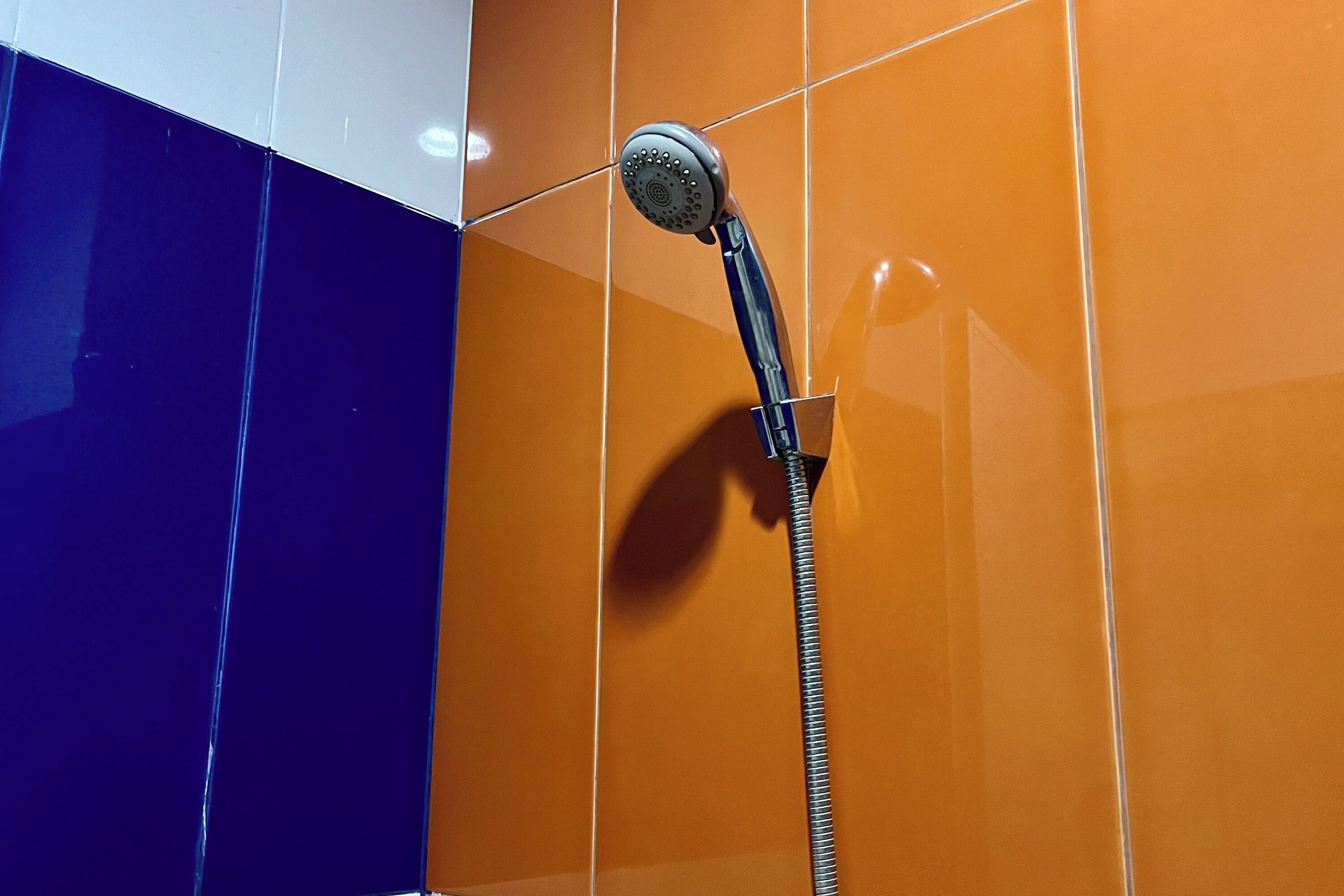 A shower with a handheld hose in a bathroom with orange and blue tiled walls.