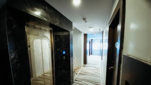 A hotel corridor with a zebra-patterned carpet, black marble walls, and a glass elevator. - Lucky Star Hotel Near Harbour Bay Batam (Batam)