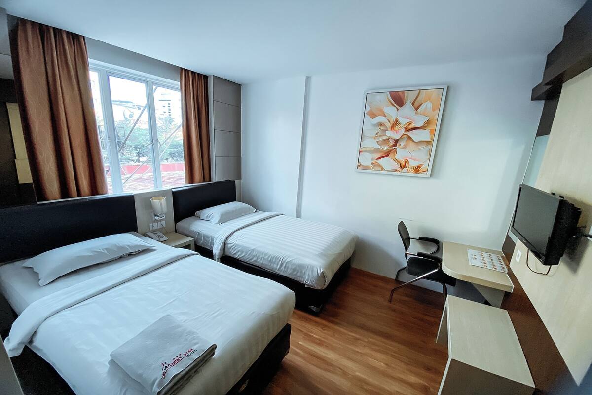 Habitación de hotel con dos camas, un escritorio, una silla, un televisor y una ventana con cortinas.