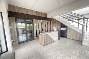 A modern reception area with a wooden reception desk, a glass door entrance, and a staircase leading to an upper level. - Keny Room @ Apt Riverdale Cikarang (Cikarang)