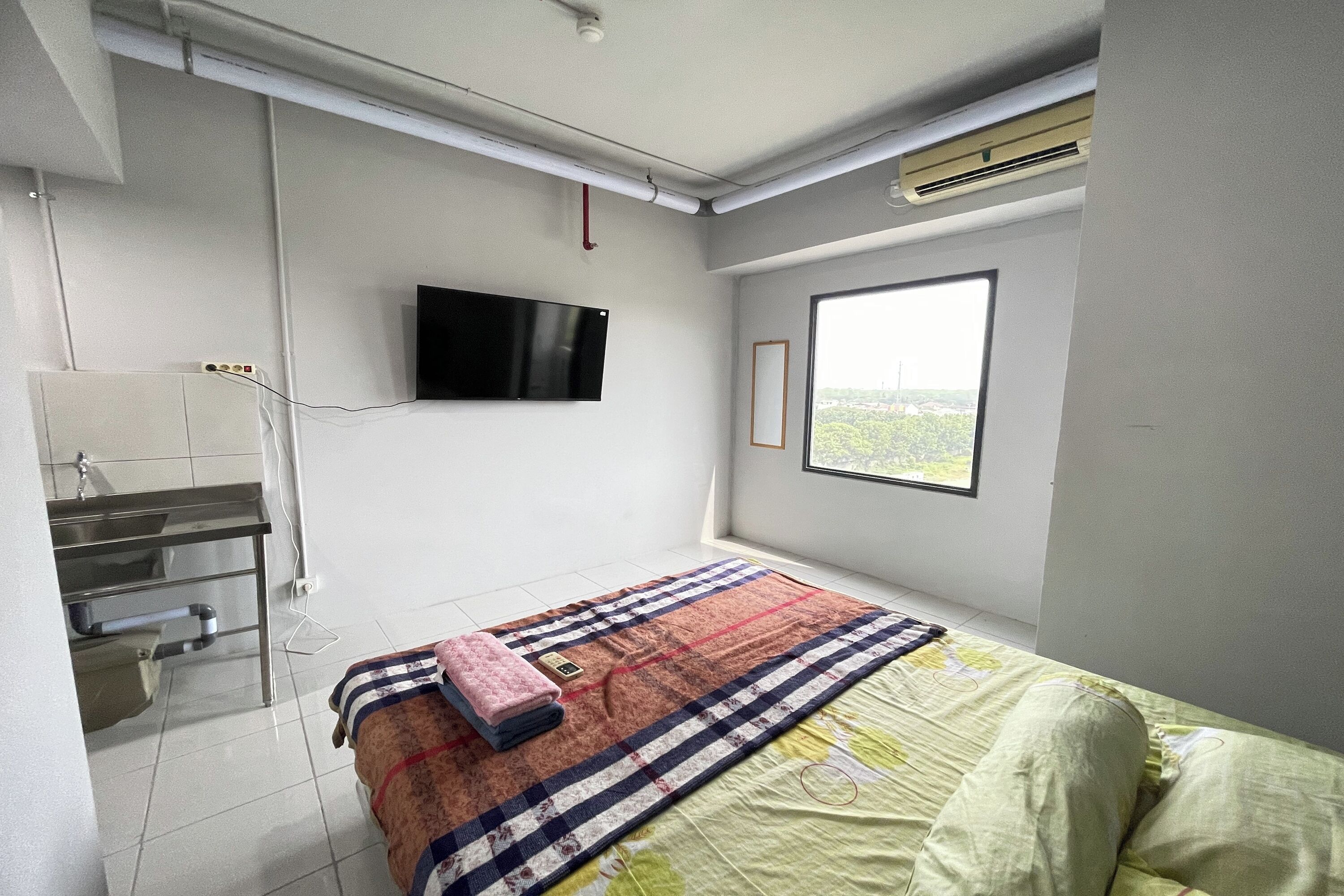 A bedroom with a bed, a TV mounted on the wall, a window, and a bathroom with a sink and mirror.