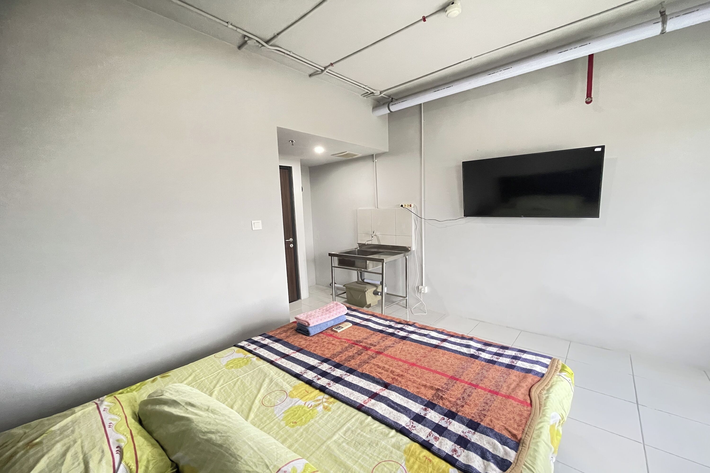 A bedroom with a bed, a desk, and a TV mounted on the wall.