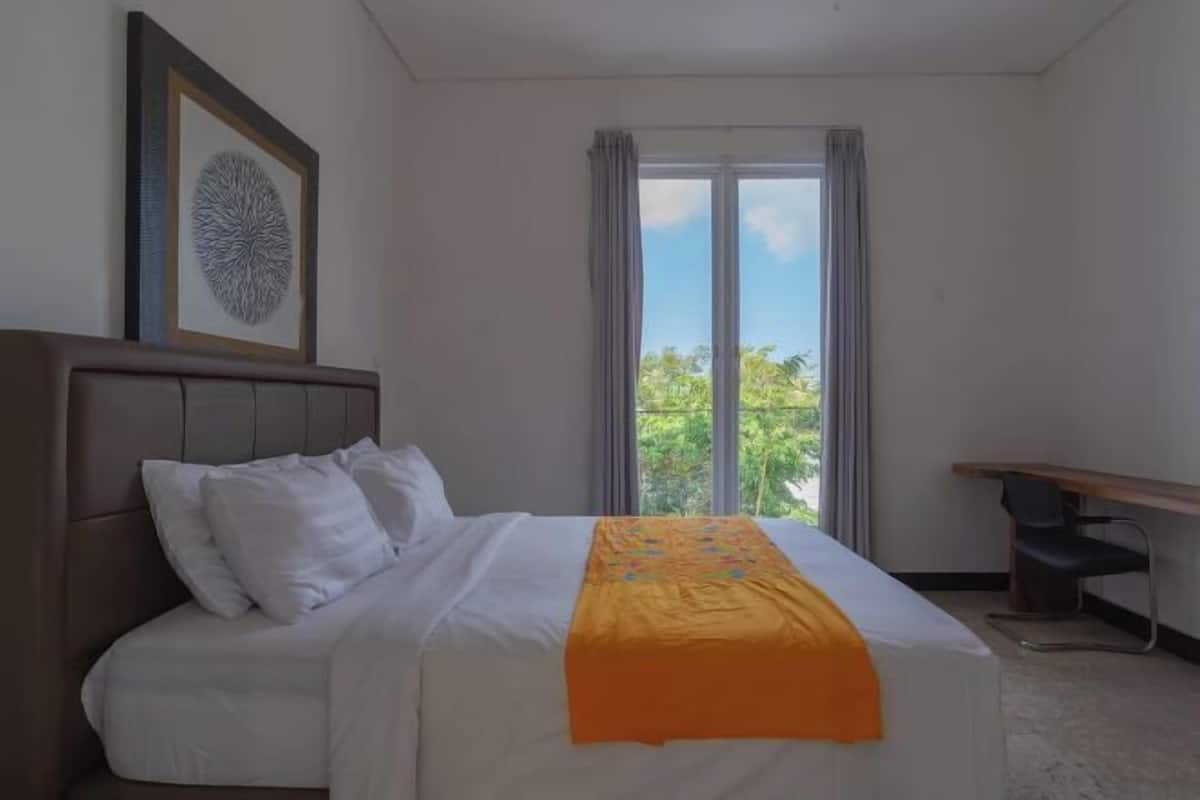 Ein Hotelzimmer mit Bett, Schreibtisch, einem Fenster mit Vorhängen und einem gerahmten Kunstwerk an der Wand.