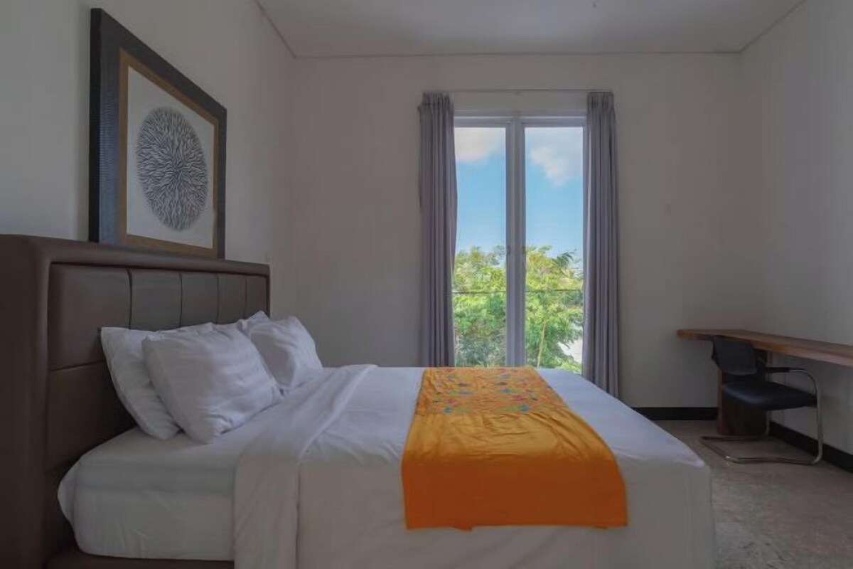 Habitación de hotel con cama, escritorio, ventana con cortinas y un cuadro en la pared.