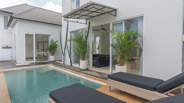 Une piscine entourée de chaises longues, de plantes en pot et d’un patio couvert.
