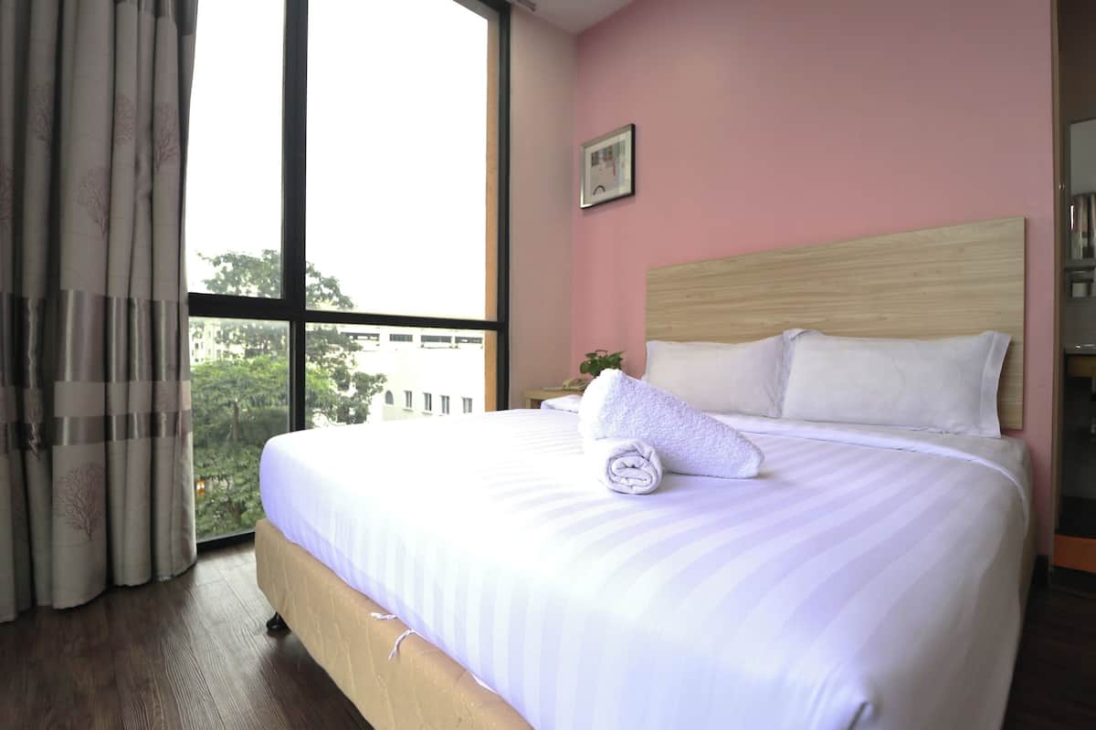 Habitación de hotel con una cama grande, una ventana con cortinas y vistas a edificios.
