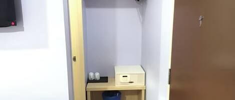 A small room with a wooden shelf, a trash bin, and a white box.