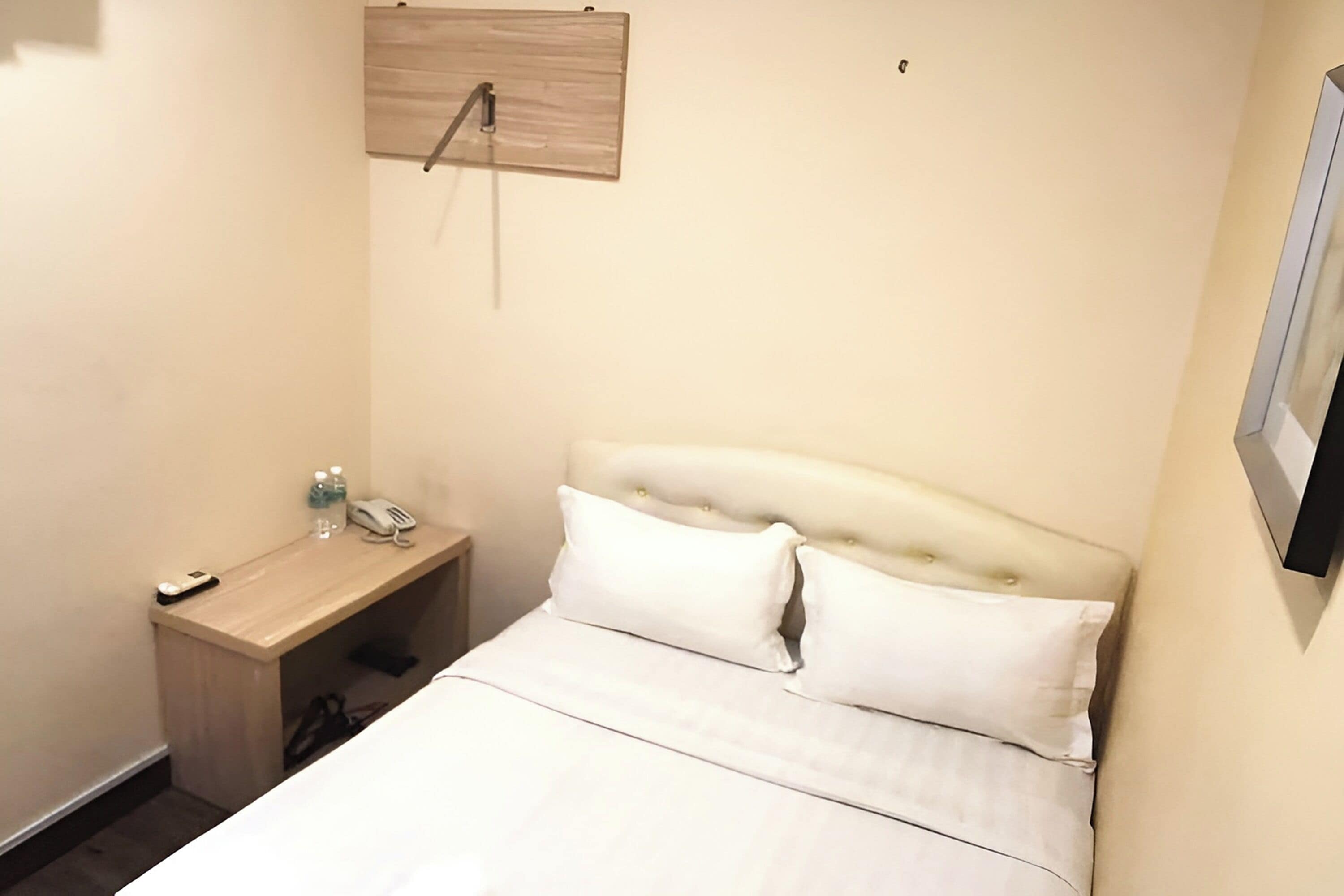 A hotel room with a bed, a bedside table with a phone and a bottle, and a wooden panel on the wall.