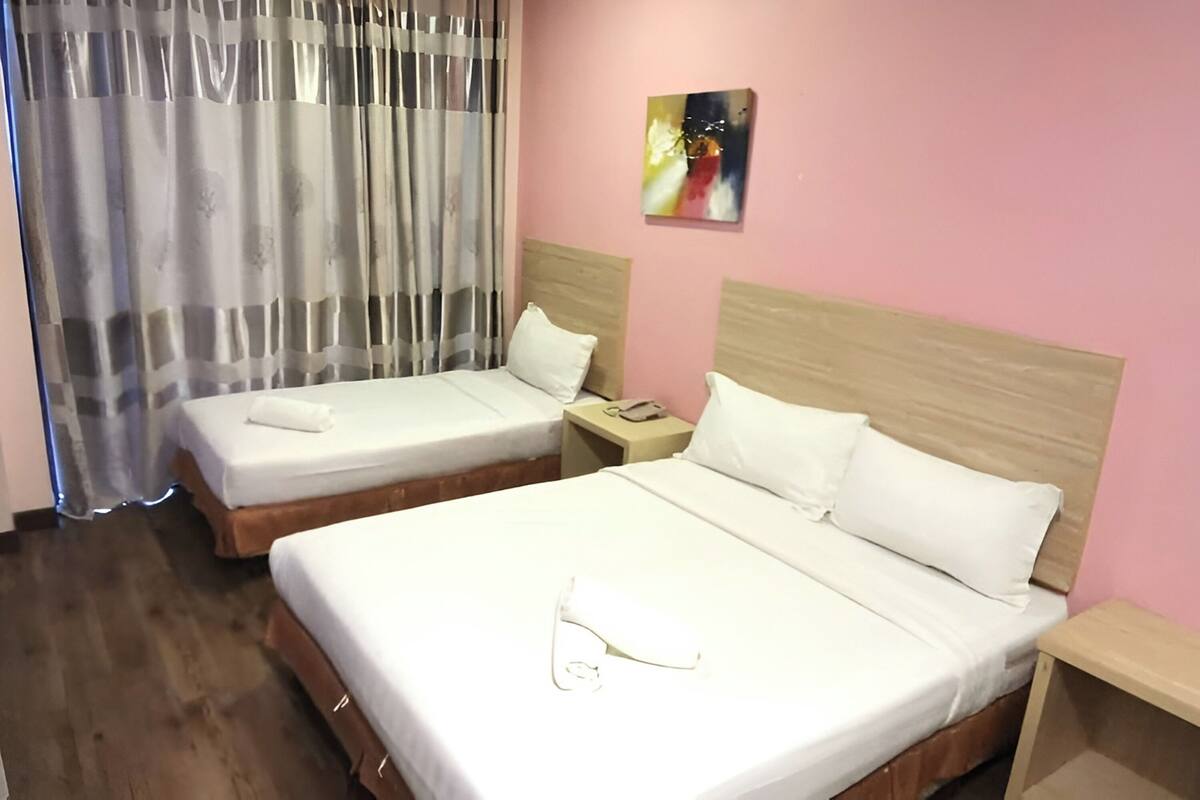 Hotellihuone, jossa on kaksi sänkyä, puinen pääty, yöpöytä, taulu ja verho.