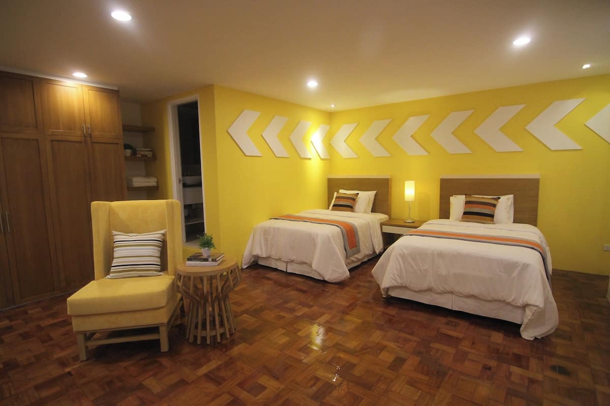 Une chambre d’hôtel avec deux lits, une chaise, une petite table et un plancher en bois.